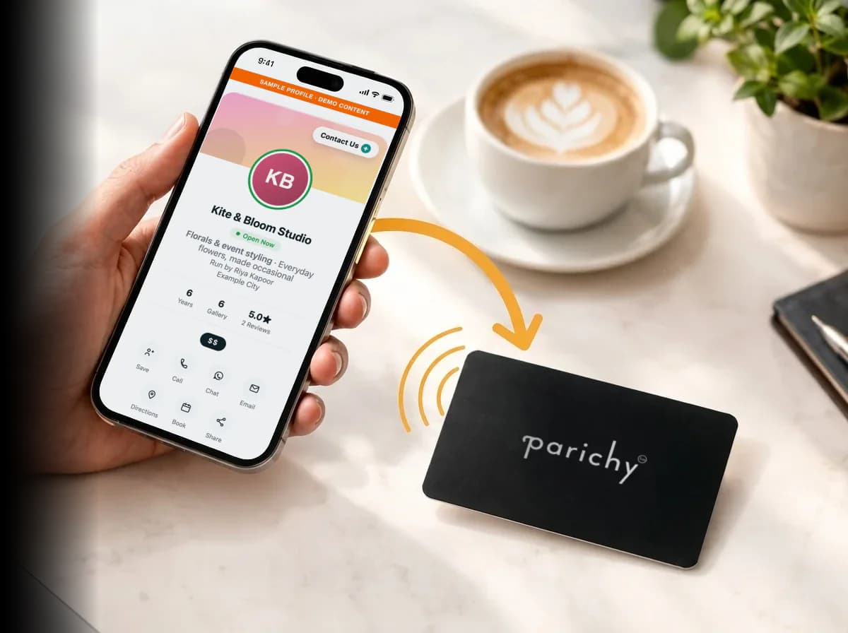 A hand holding a smartphone that shows a sample Smart Profile — Kite & Bloom Studio, a florist — beside a Parichy NFC card on a desk